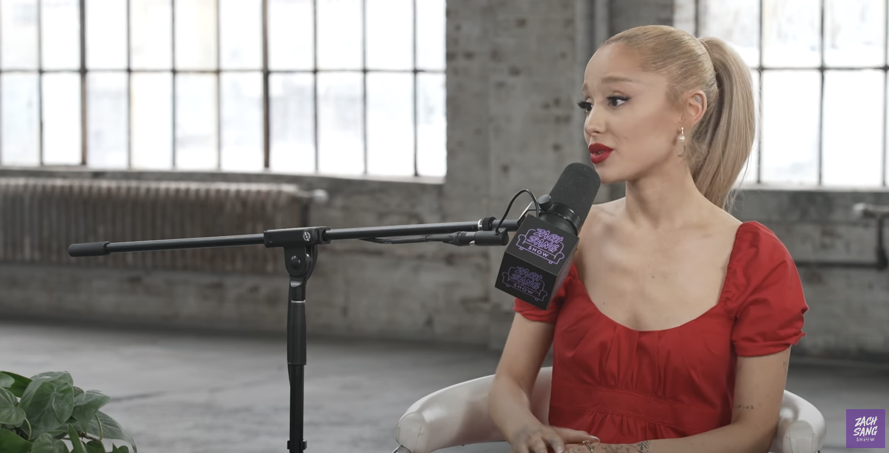 Ariana Grande in an interview wearing a dress with puffed sleeves, sitting in a warehouse