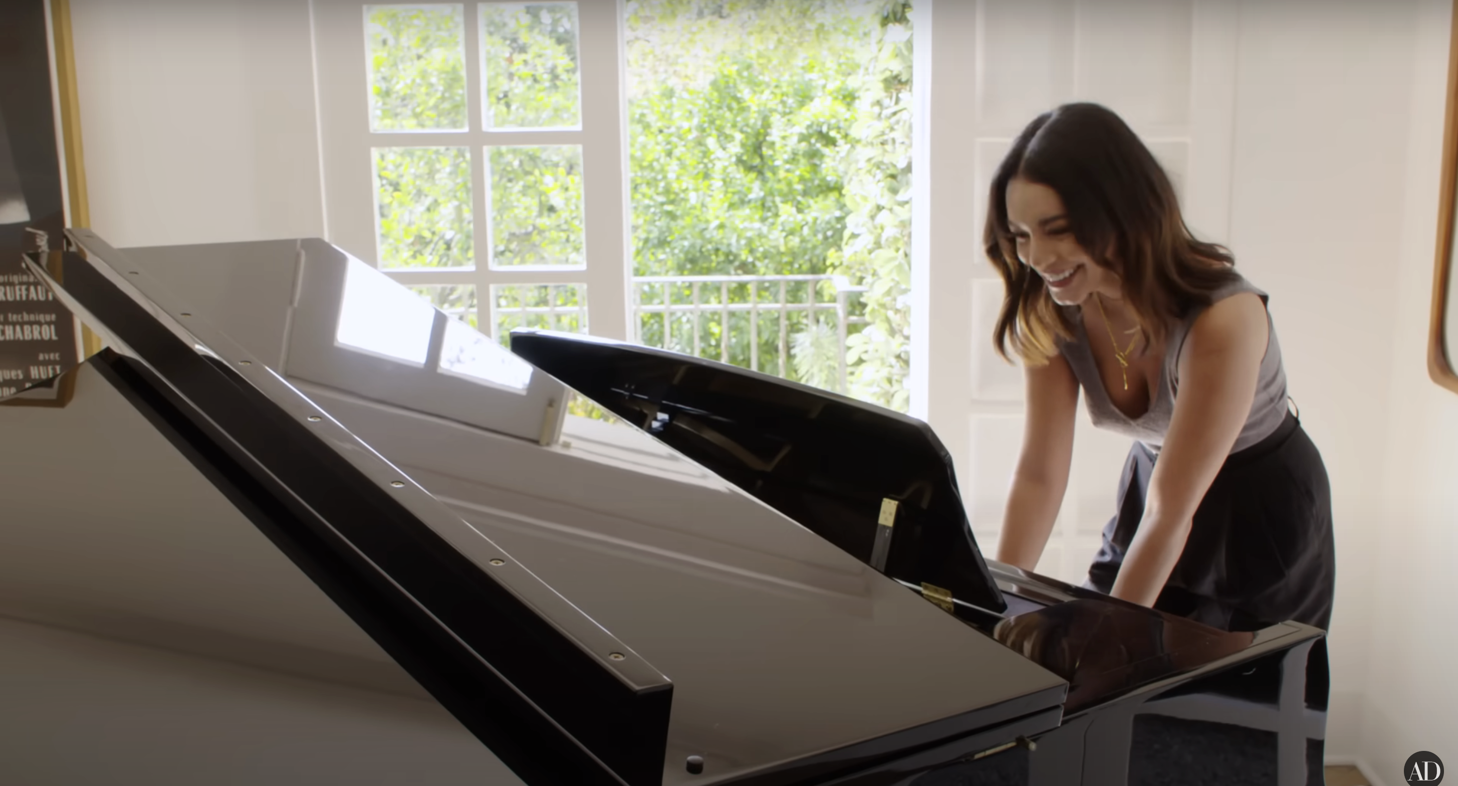 Vanessa Hudgens smiles while playfully posing with a grand piano in a sunlit room