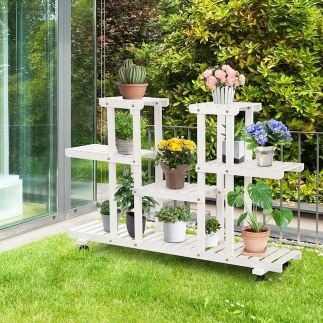 White multi-tiered garden shelf with various potted plants, placed on a lawn near glass doors