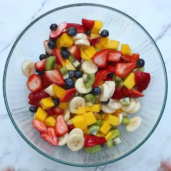 A bowl filled with a variety of fresh fruit, including strawberries, bananas, kiwi, and mango