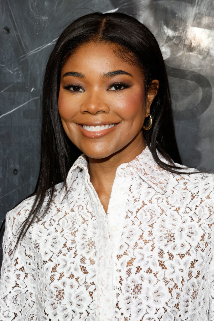 Gabrielle Union smiling in a white lace blouse with hoop earrings at an event