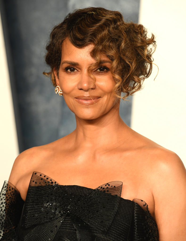 Halle posing at an event, wearing an elegant black outfit with a sheer neckline with curled short hair