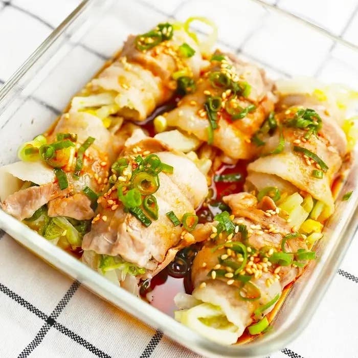皿に盛られた豚バラ肉の蒸し白菜、ネギとごまがトッピングされている。