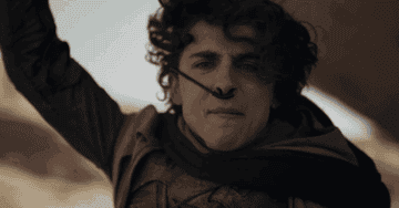 Character Paul Atreides raises hand with intense expression in a desert scene from Dune