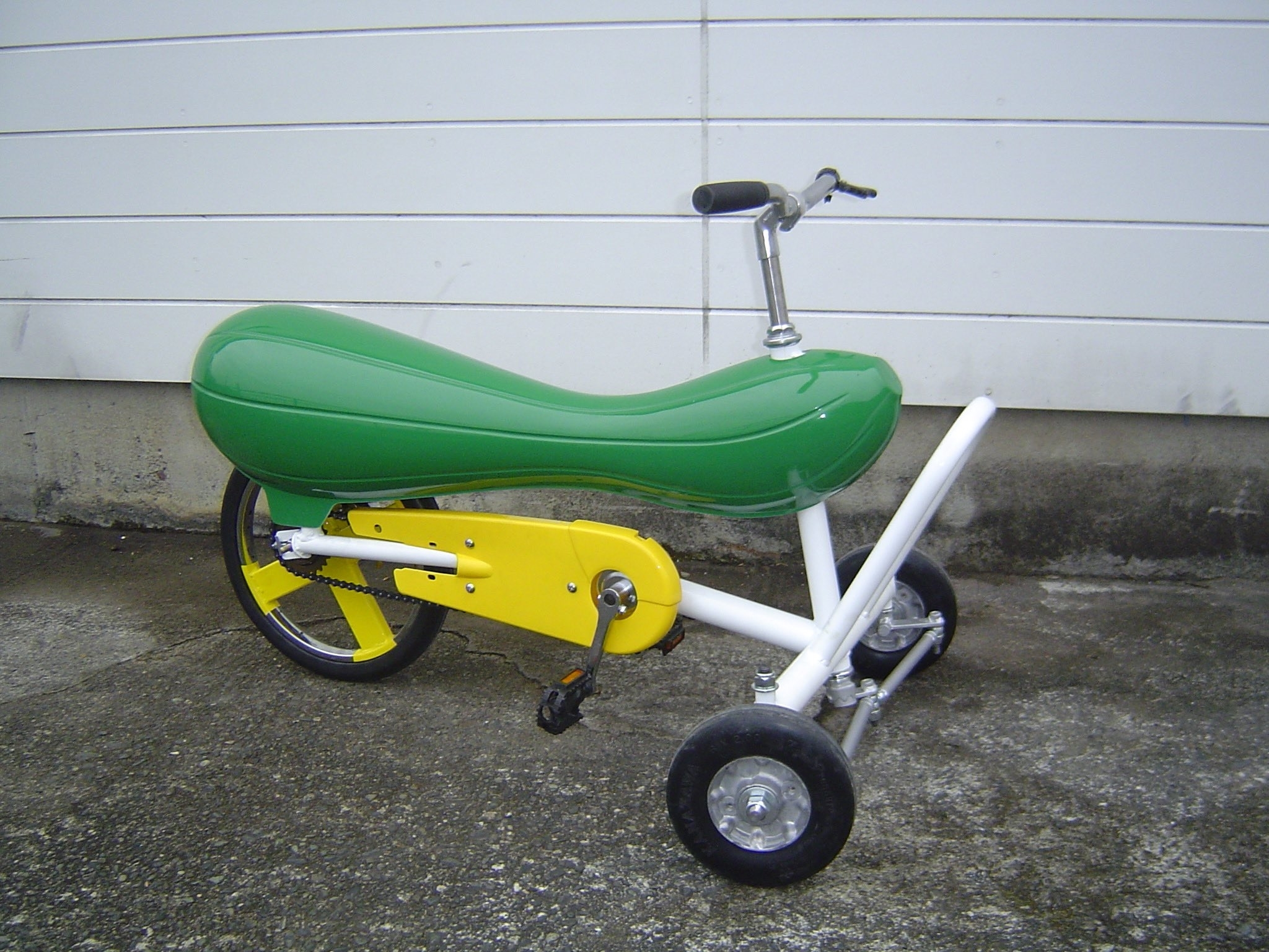 緑の座席がある黄色い子供用の三輪車がコンクリートの地面に置かれています。