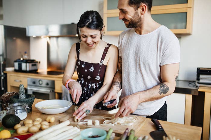 Two people cooking together in a kitchen, smiling as they prepare food
