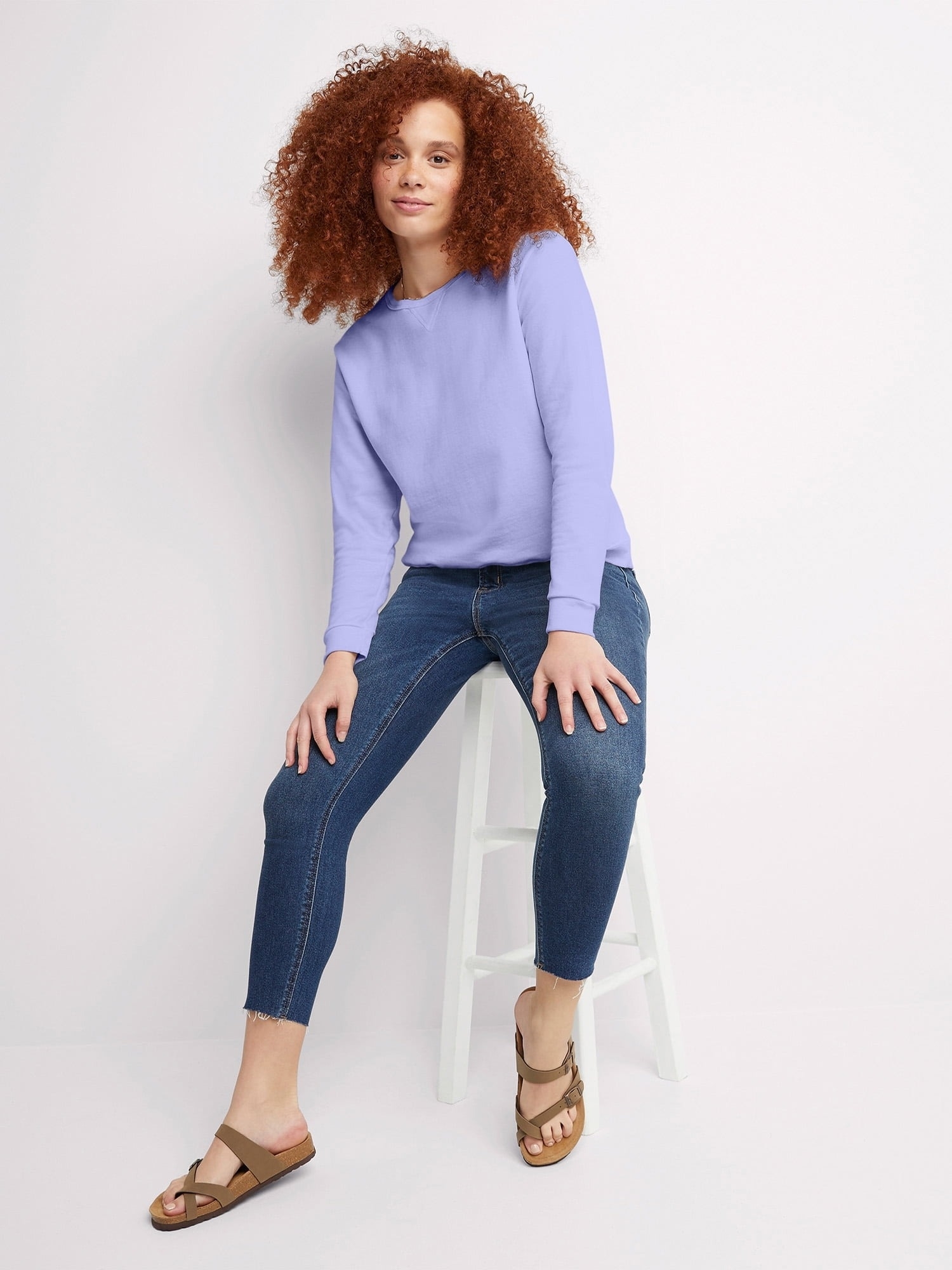 model in a long-sleeve periwinkle top and jeans sitting on a stool