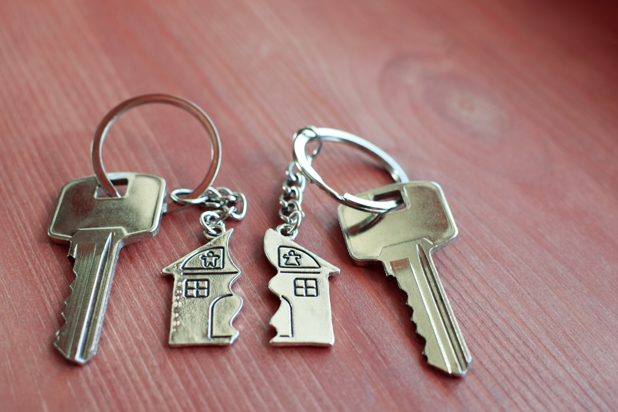 Two keychains with house-shaped pendants and keys on a wooden surface, symbolizing cohabitation or shared living spaces