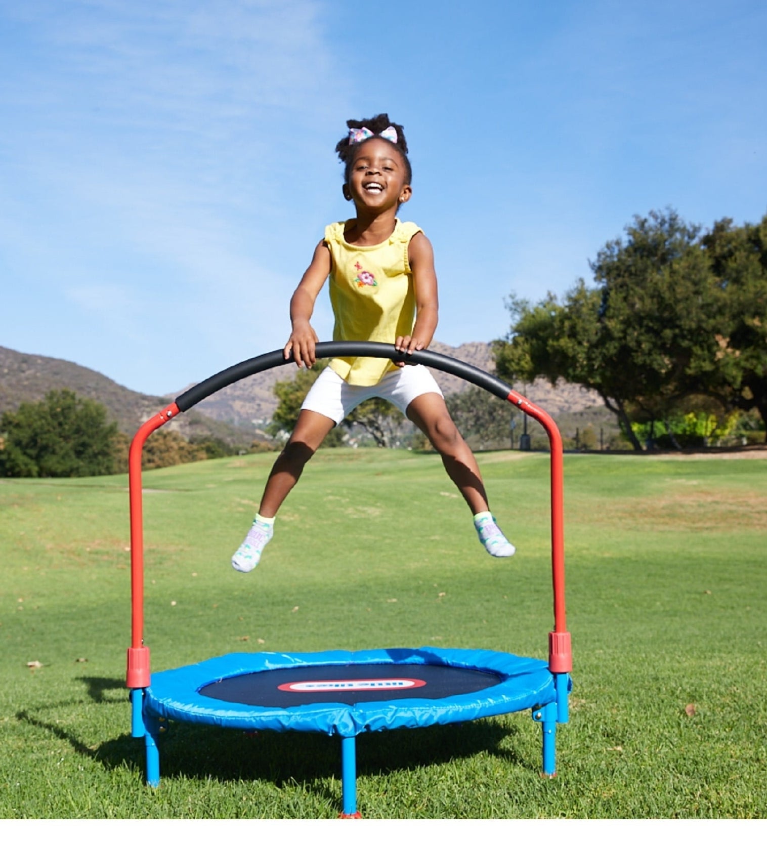 Child jumps on outdoor trampoline with handlebar in a sunny grassy area