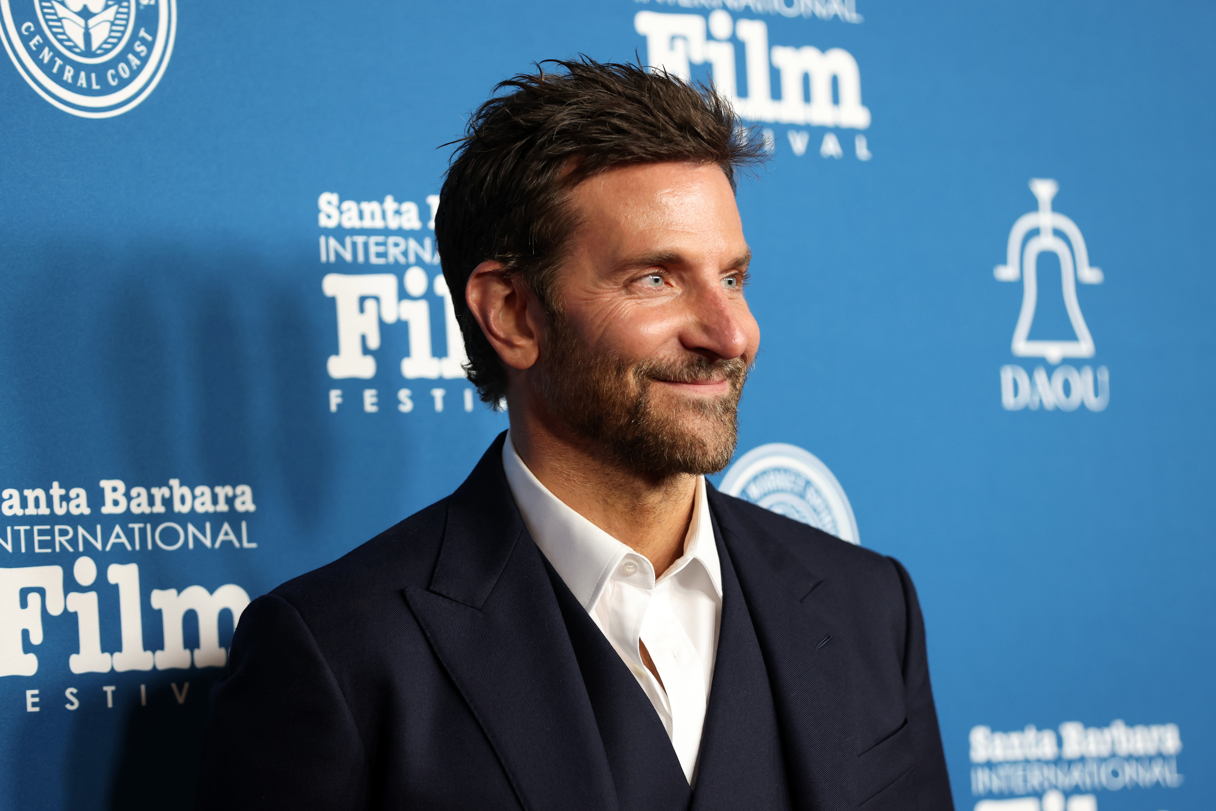 Bradley in suit smiling at an event, style evident, on a branded background