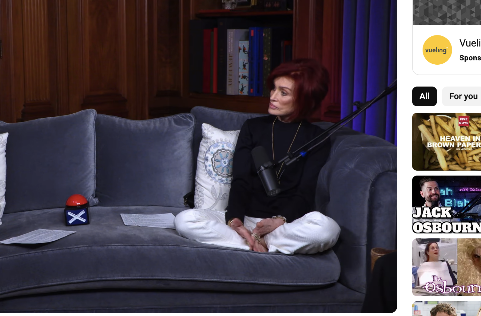 Two people sitting on a couch during an interview, with one wearing a black shirt and the other a white hoodie