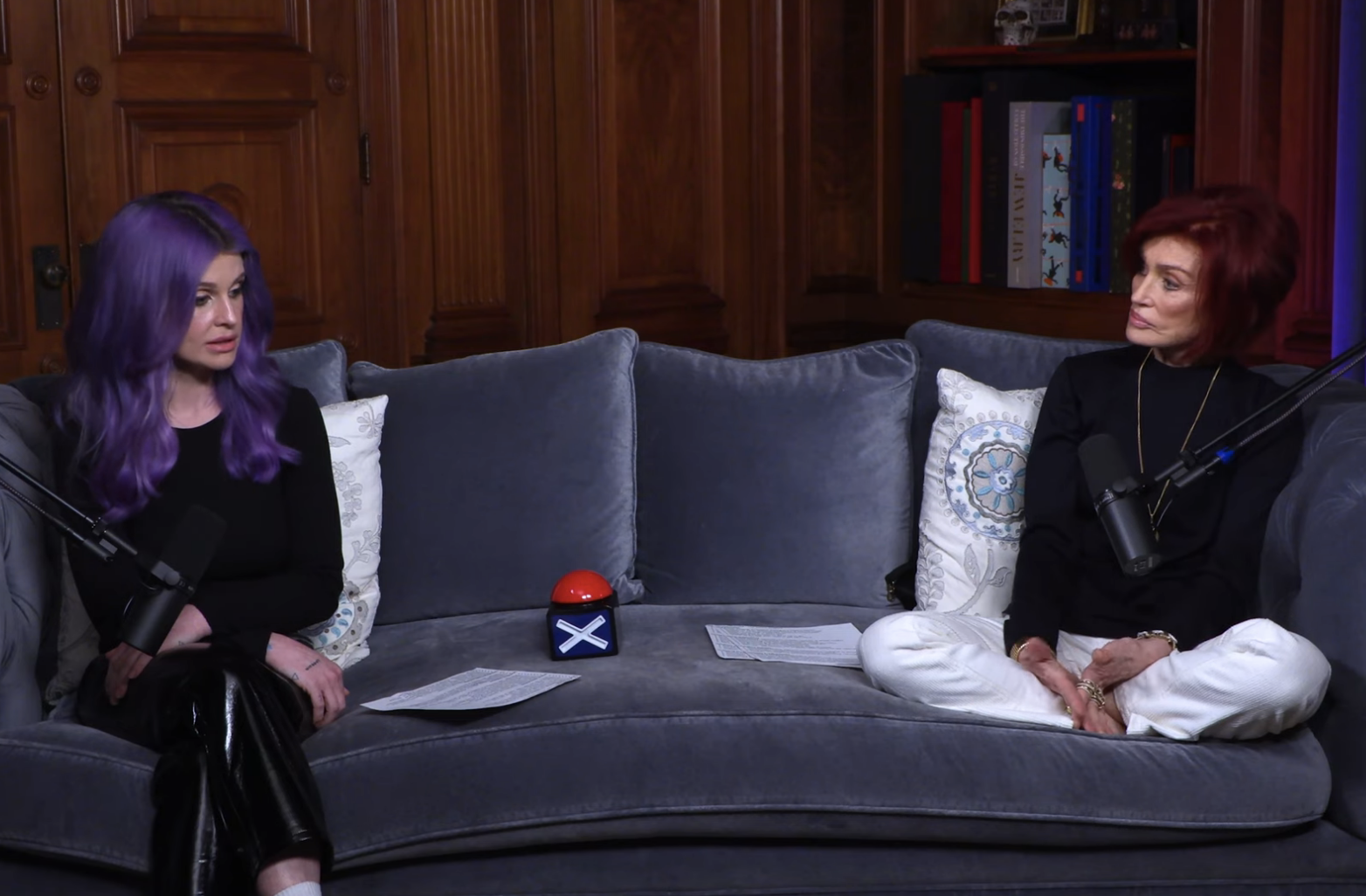 Two people sitting on a couch during an interview, with one wearing a black shirt and the other a white hoodie