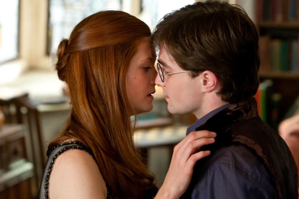 Ginny Weasley and Harry Potter characters share a close moment. Ginny, with hair up, touches Harry&#x27;s face. They are indoors