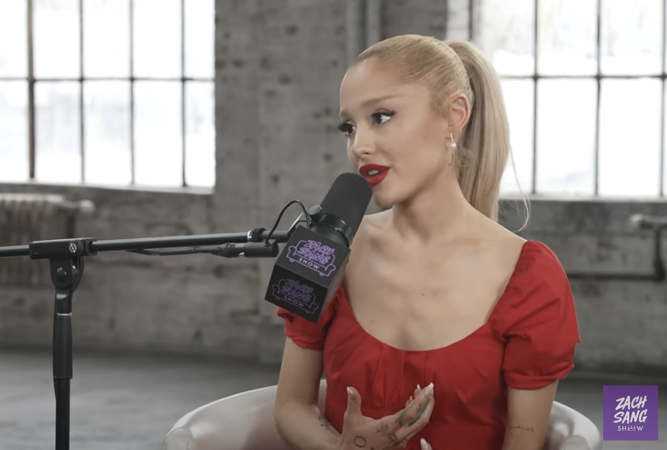 Ariana Grande in a puff-sleeve dress speaking into a microphone during an interview