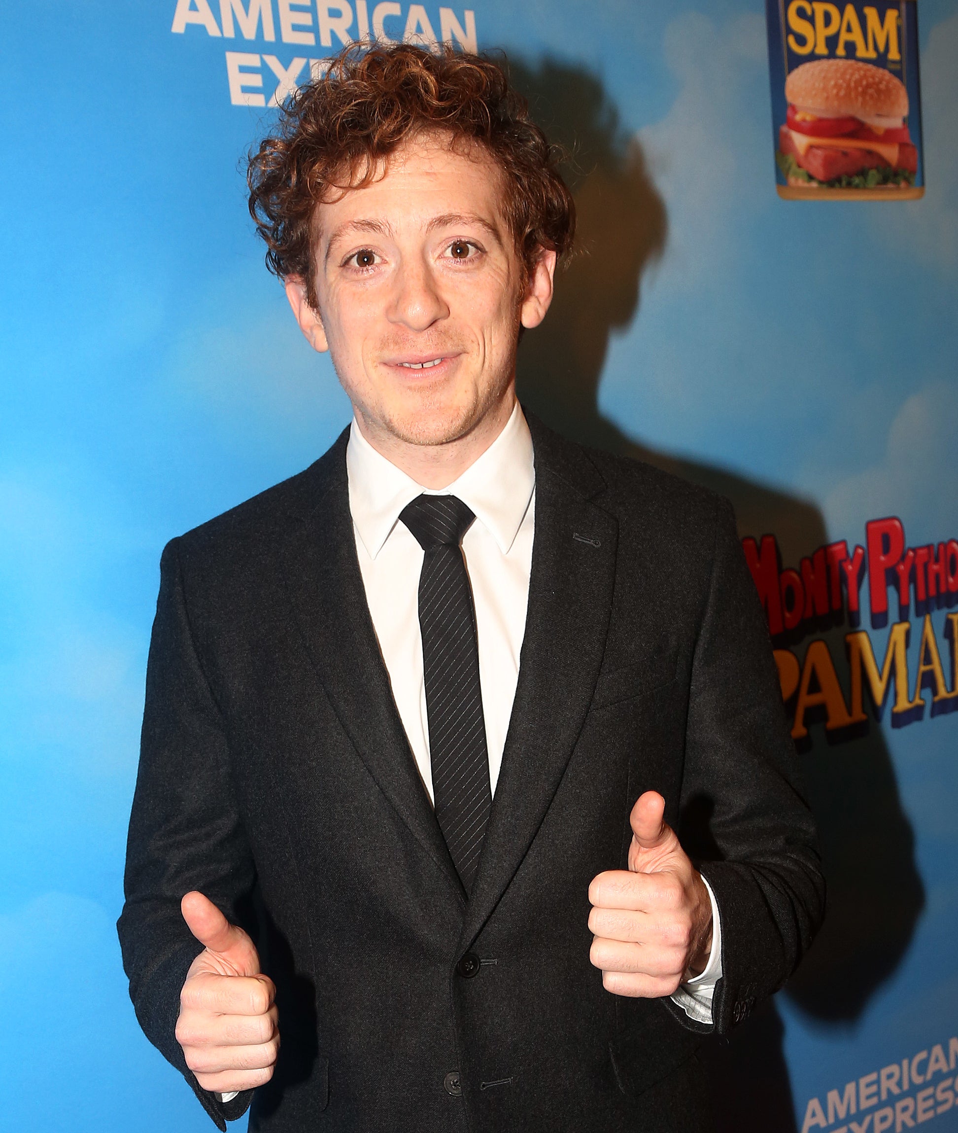 Ethan Slater in suit and tie gives thumbs up at an event