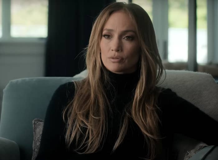 Jennifer Lopez in a turtleneck sitting on a couch, looking thoughtful