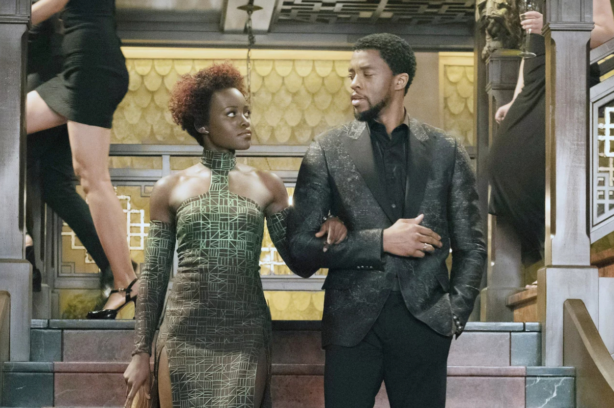 Two characters from a movie, a man and a woman, are standing side by side in textured, formal attire