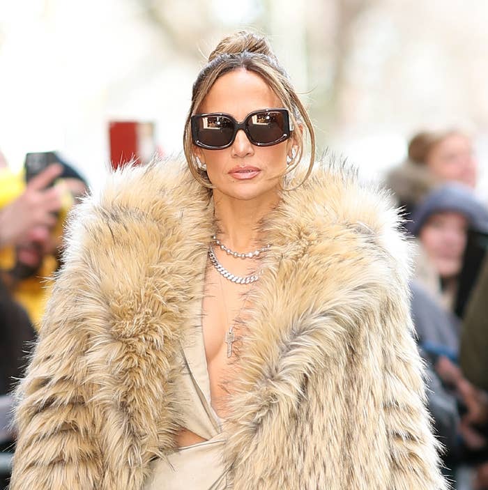 Jennifer Lopez in a fur coat and sunglasses, walking with photographers in background