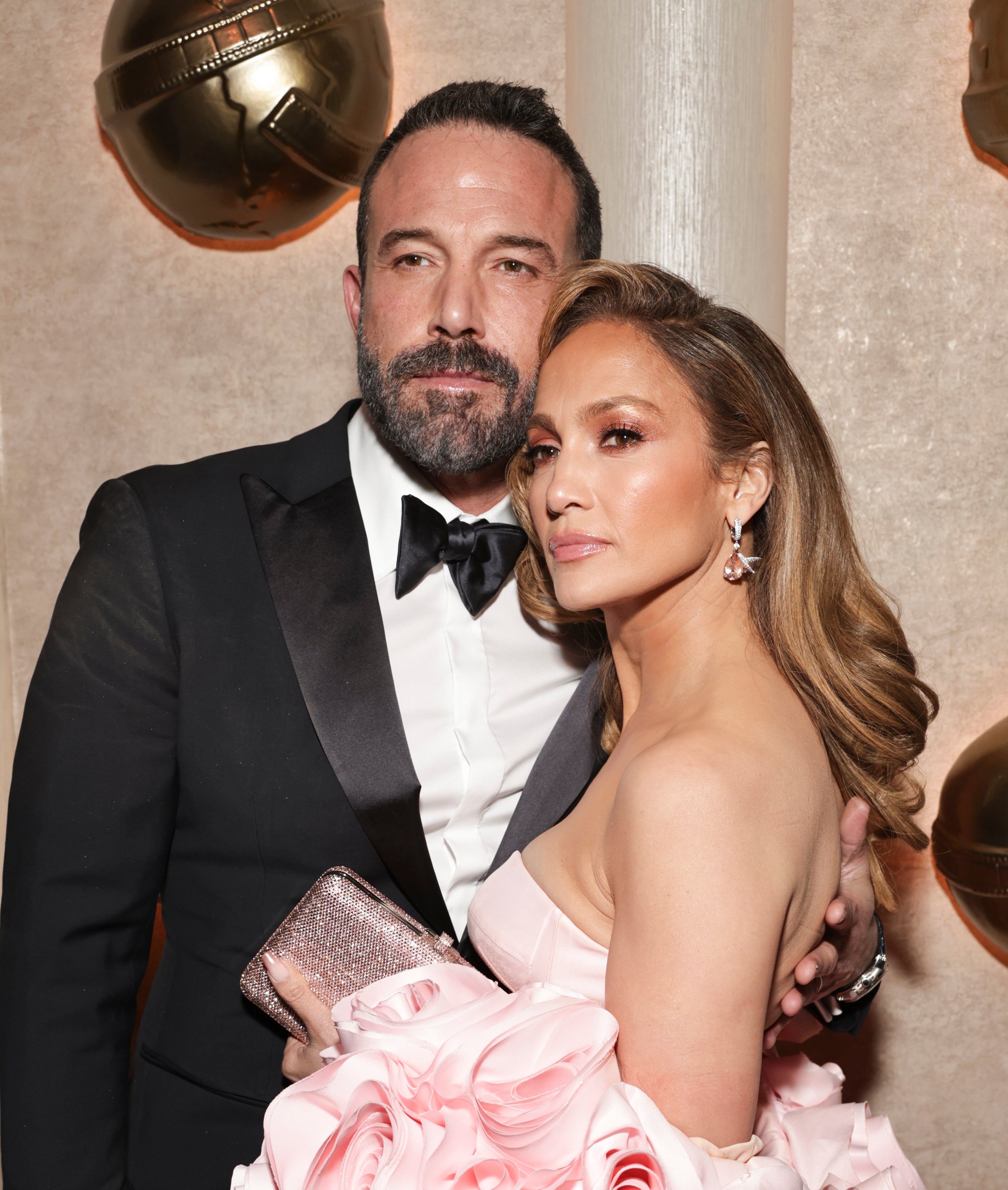 Jennifer Lopez in a gown with floral embellishments poses with Ben Affleck in a tuxedo