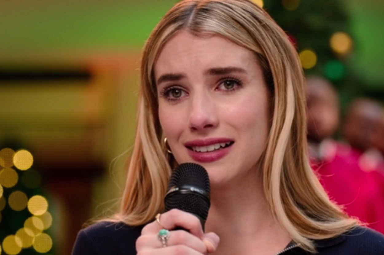 Emma Roberts wearing a ring, holds a microphone, emotional expression with blurred background