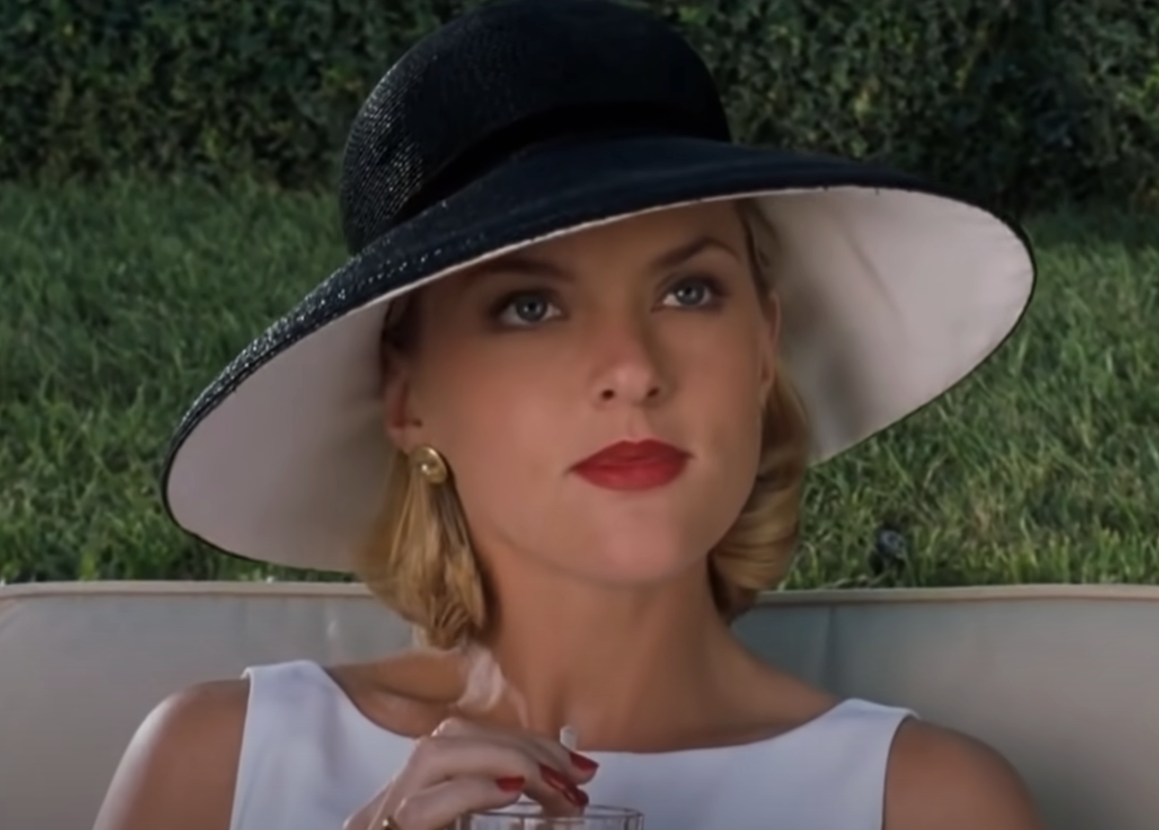 Woman in wide-brimmed hat sipping a drink, poised elegantly, from a classic film scene