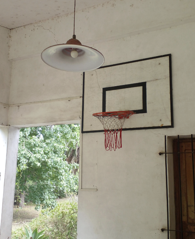 Basketball hoop mounted on a wall with a hanging lamp above, in an outdoor covered area