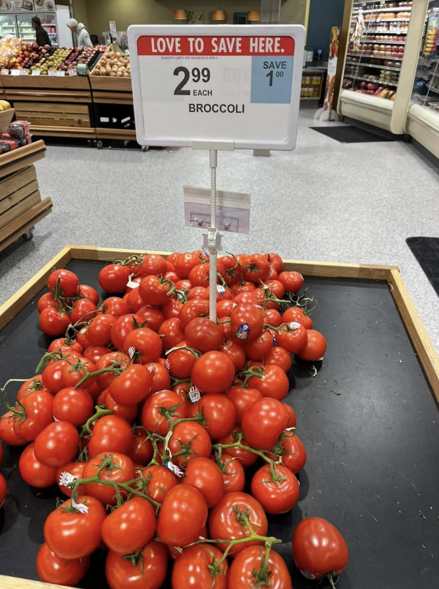 Tomatoes on sale in a grocery store, with a misplaced sign for broccoli above
