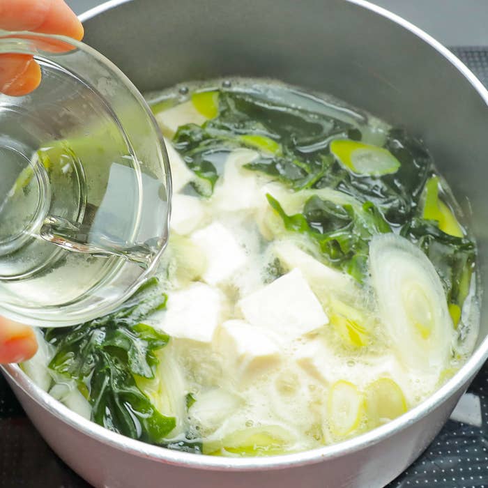 野菜と豆腐が入った鍋にみりんを注ぐ手。