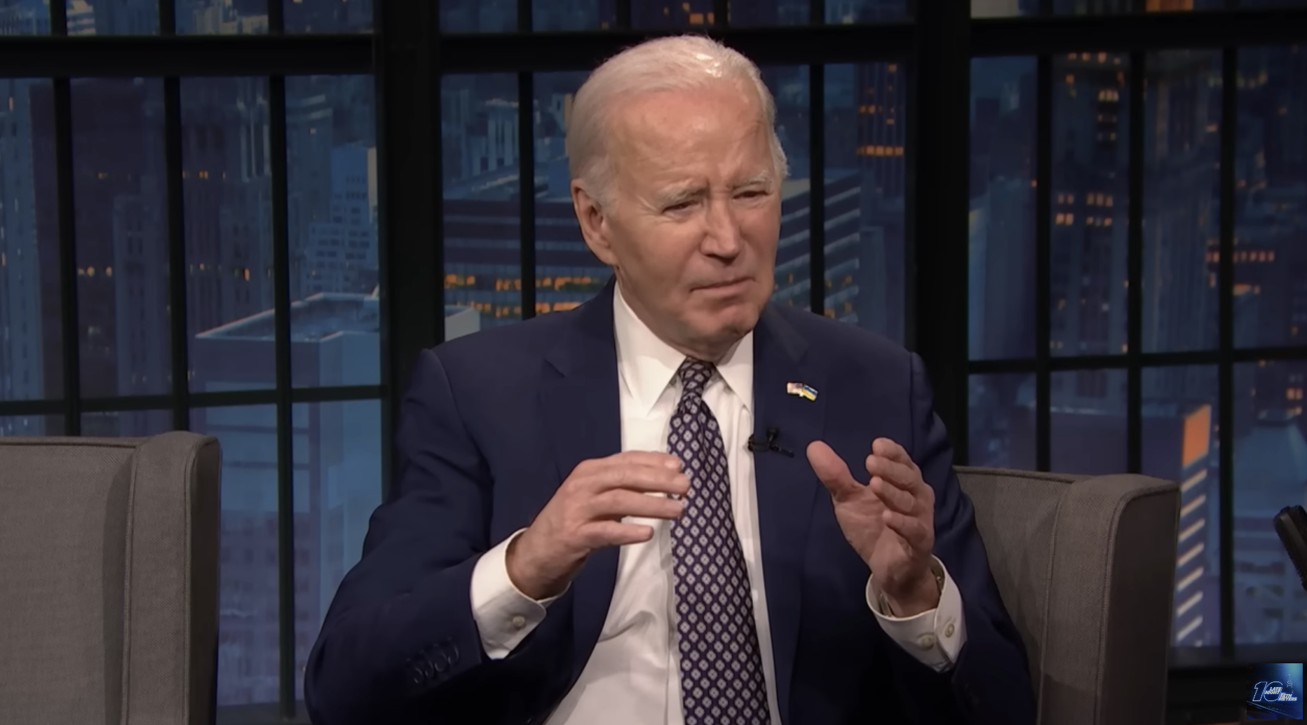 Joe Biden seated, gesturing while speaking, wearing a suit and tie, on a talk show set