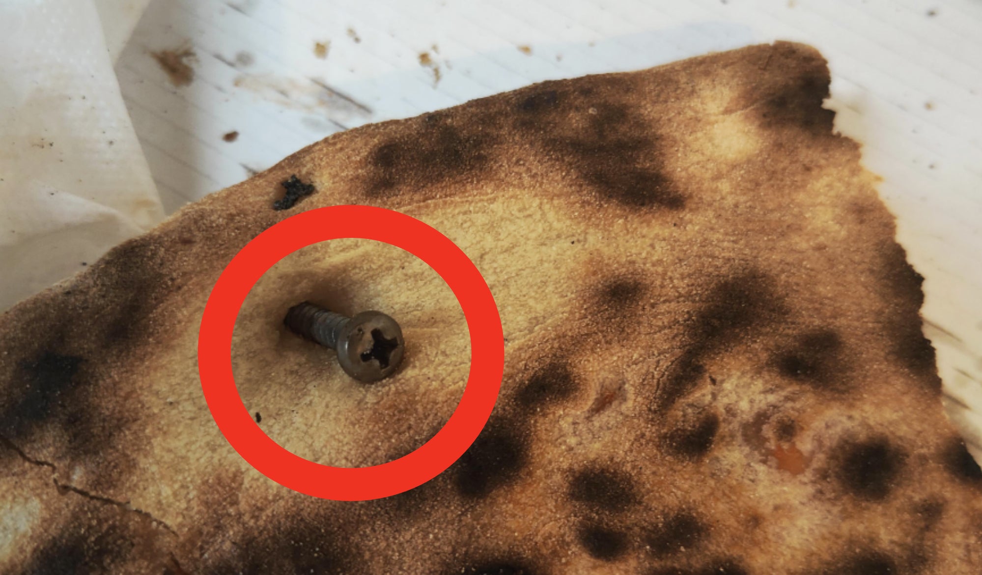 A close-up of the burnt pizza with a drawn circle highlighting the screw