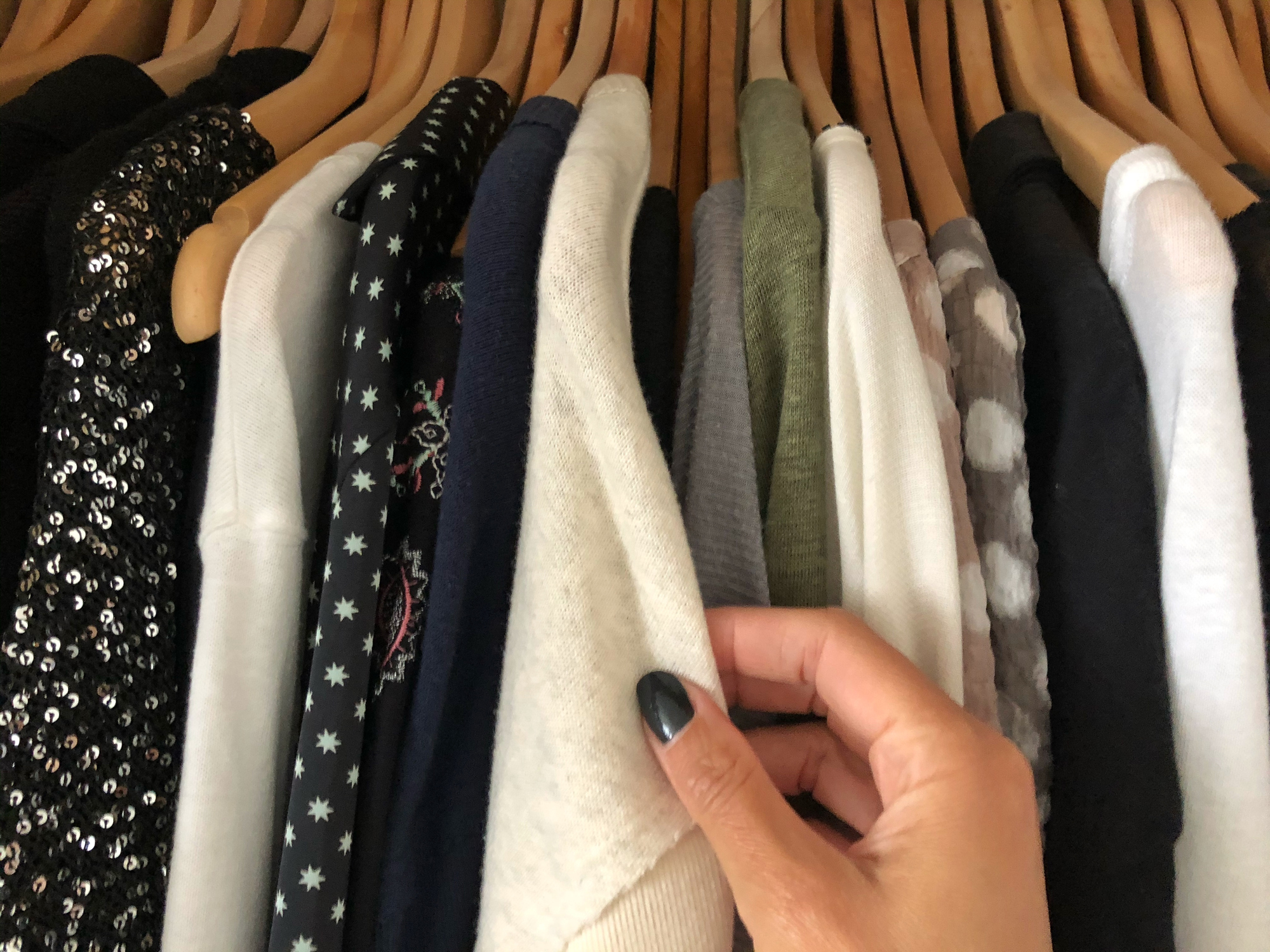 Person&#x27;s hand browsing through a variety of clothes on hangers