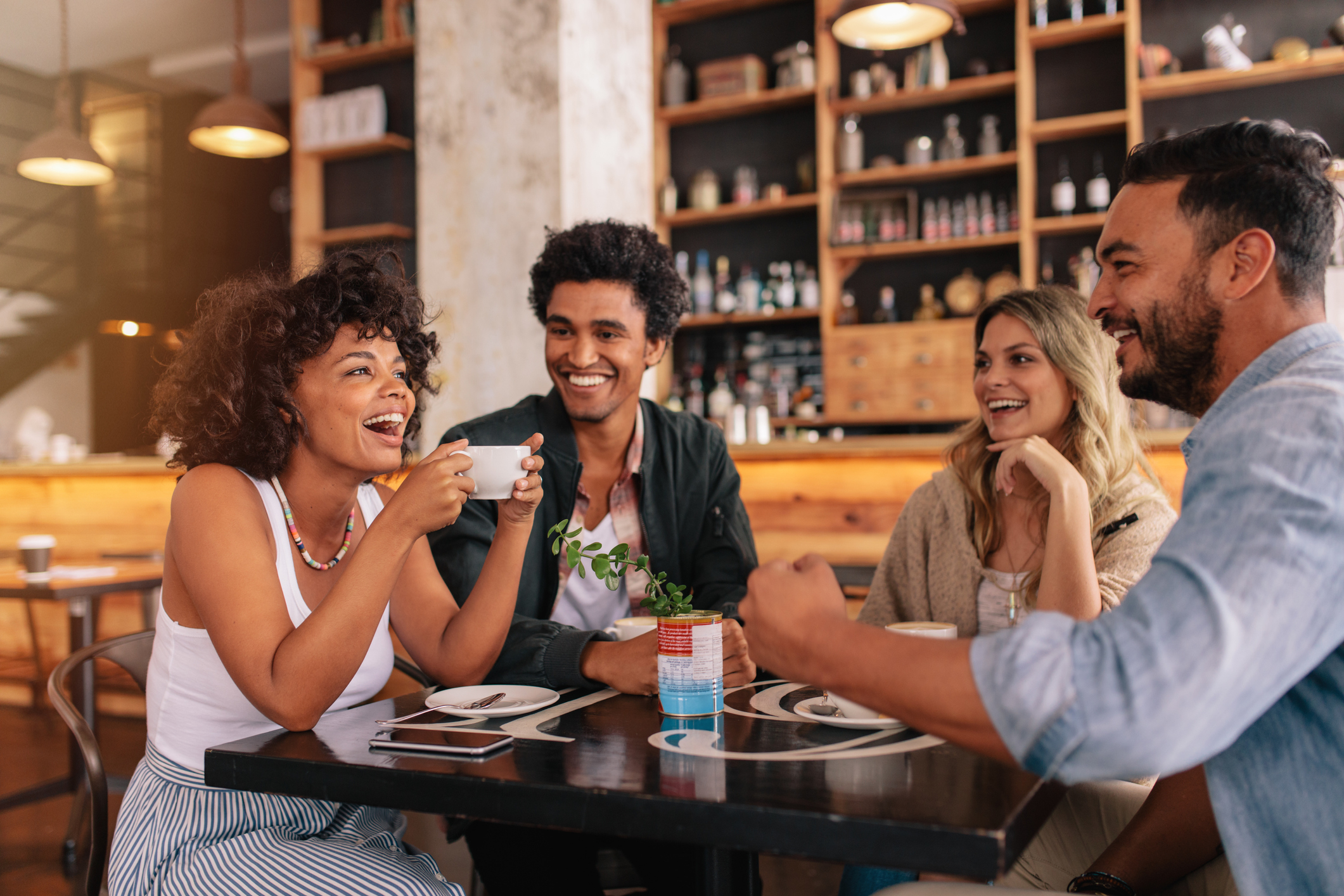 Four friends laughing and enjoying coffee together at a cafe table
