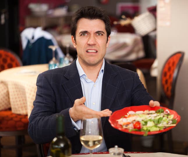 Man at a restaurant table, appearing displeased with the salad on his plate