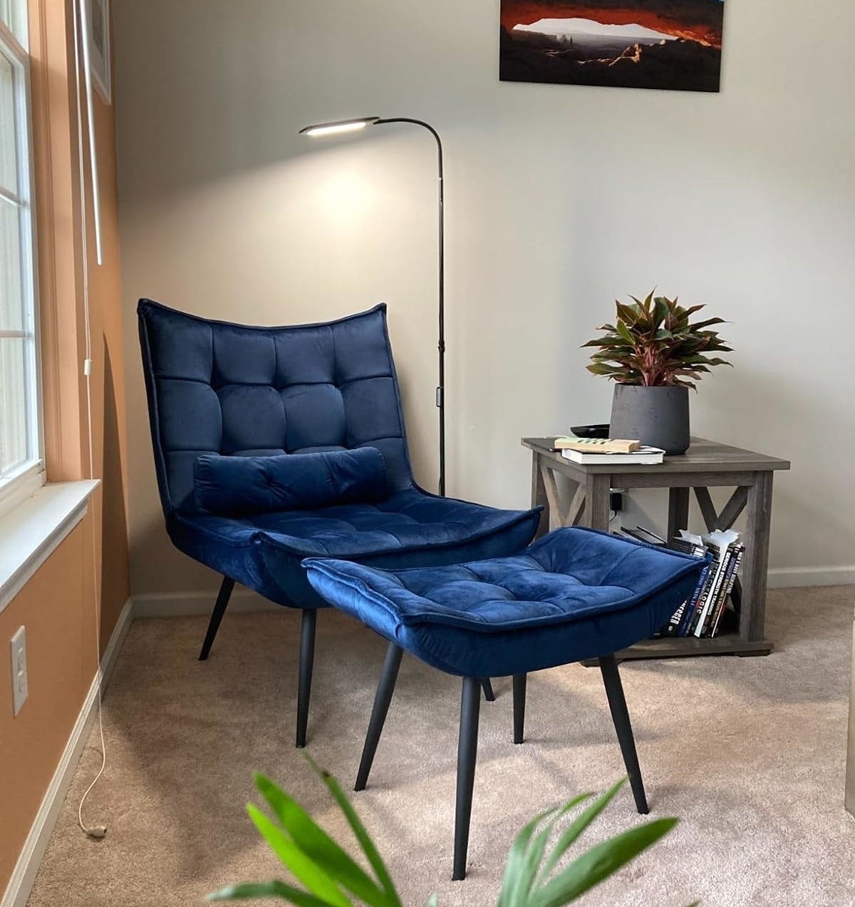 A cozy reading nook with an adjustable floor lamp and a tufted blue lounge chair next to a wooden side table with a plant