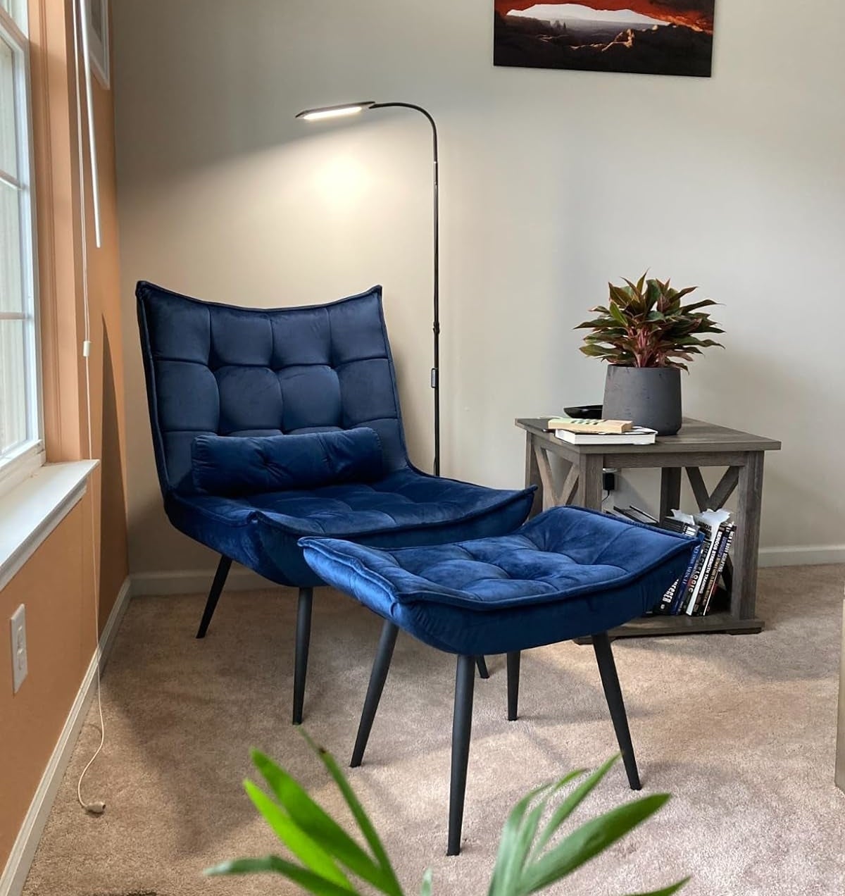 A cozy reading nook with an adjustable floor lamp and a tufted blue lounge chair next to a wooden side table with a plant