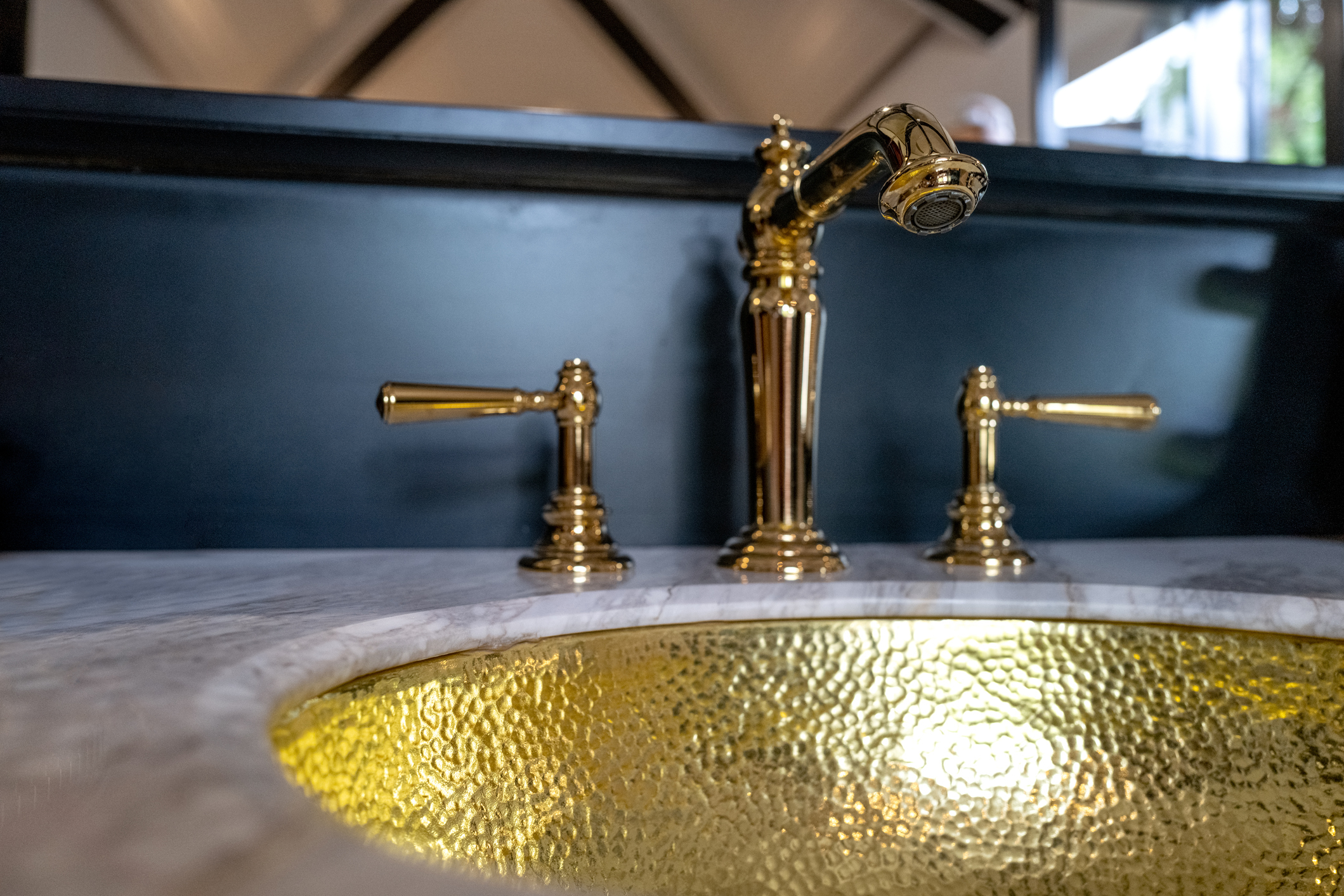 Brass faucet over a textured sink, reflecting light, set in a stone countertop