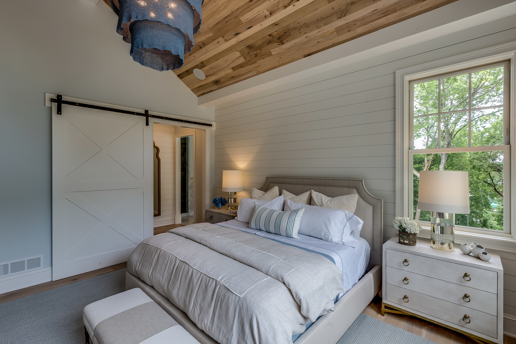 Rustic bedroom with a barn door, beamed ceiling, and a neatly made bed