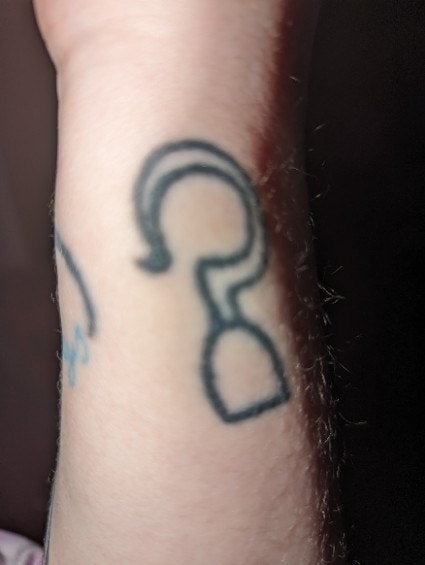 Close-up of a person&#x27;s wrist with a black ink tattoo of a question mark