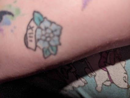 Close-up of a tattoo depicting a flower with leaves on skin, partially obscured by clothing