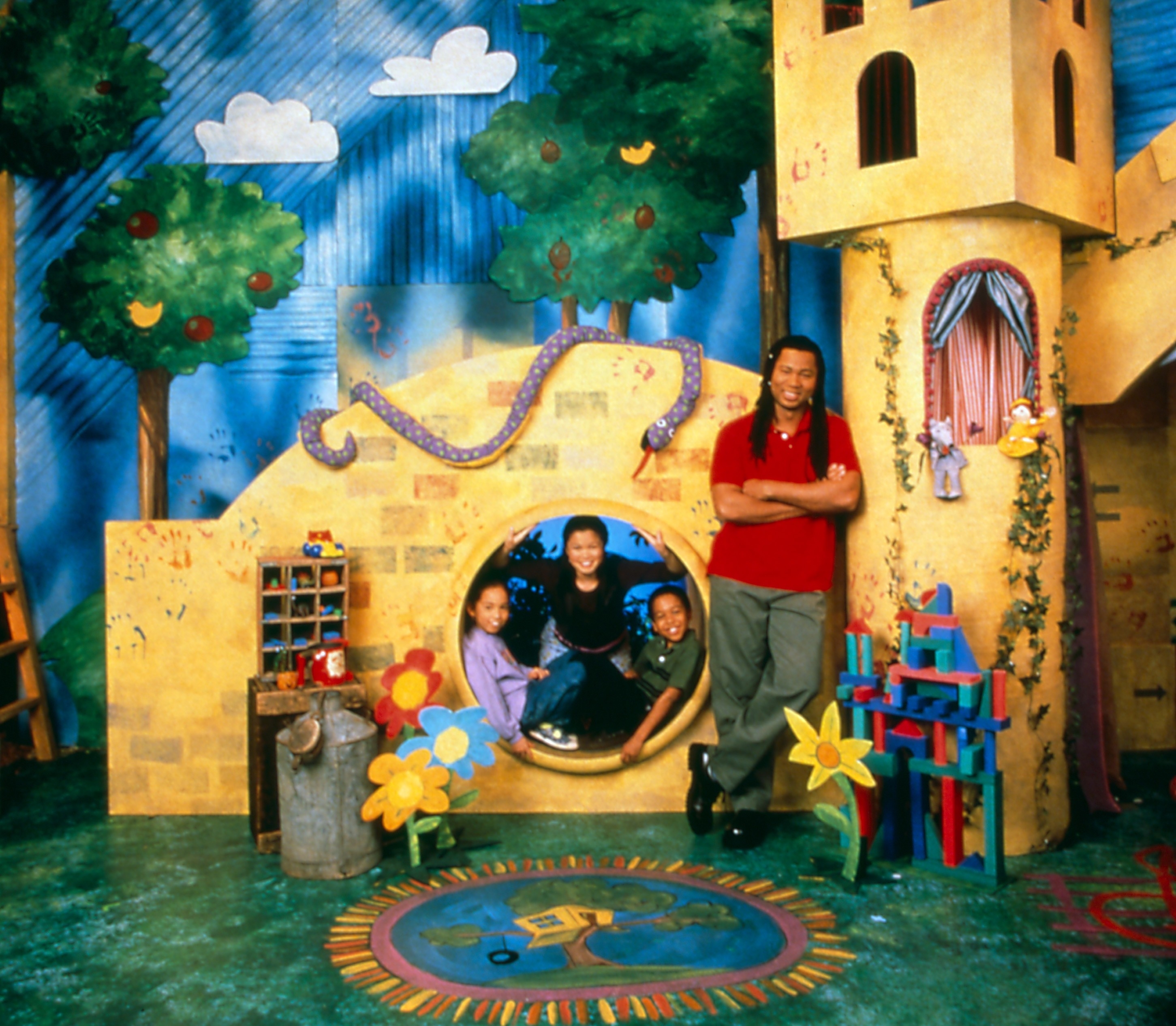 A scene from a children&#x27;s TV show with characters posing in a playful, colorful indoor set designed to look like a storybook village