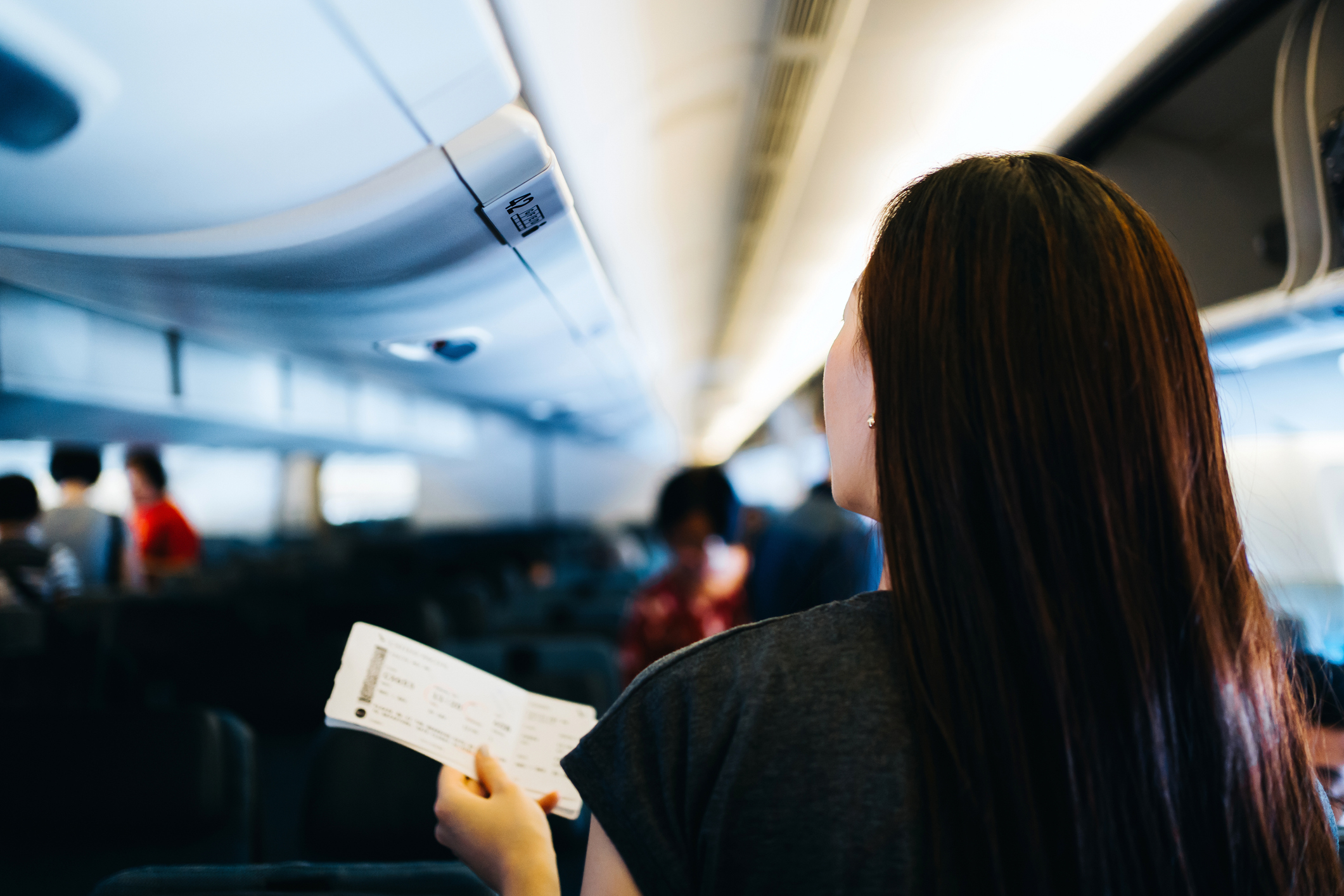 Woman inside an airplane looking at her seat ticket with passengers in the background