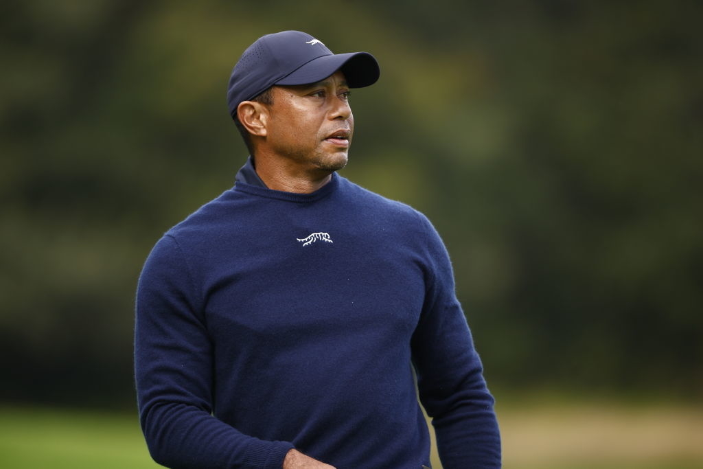 Tiger Woods wearing a sweater and cap, looking focused at a golf event