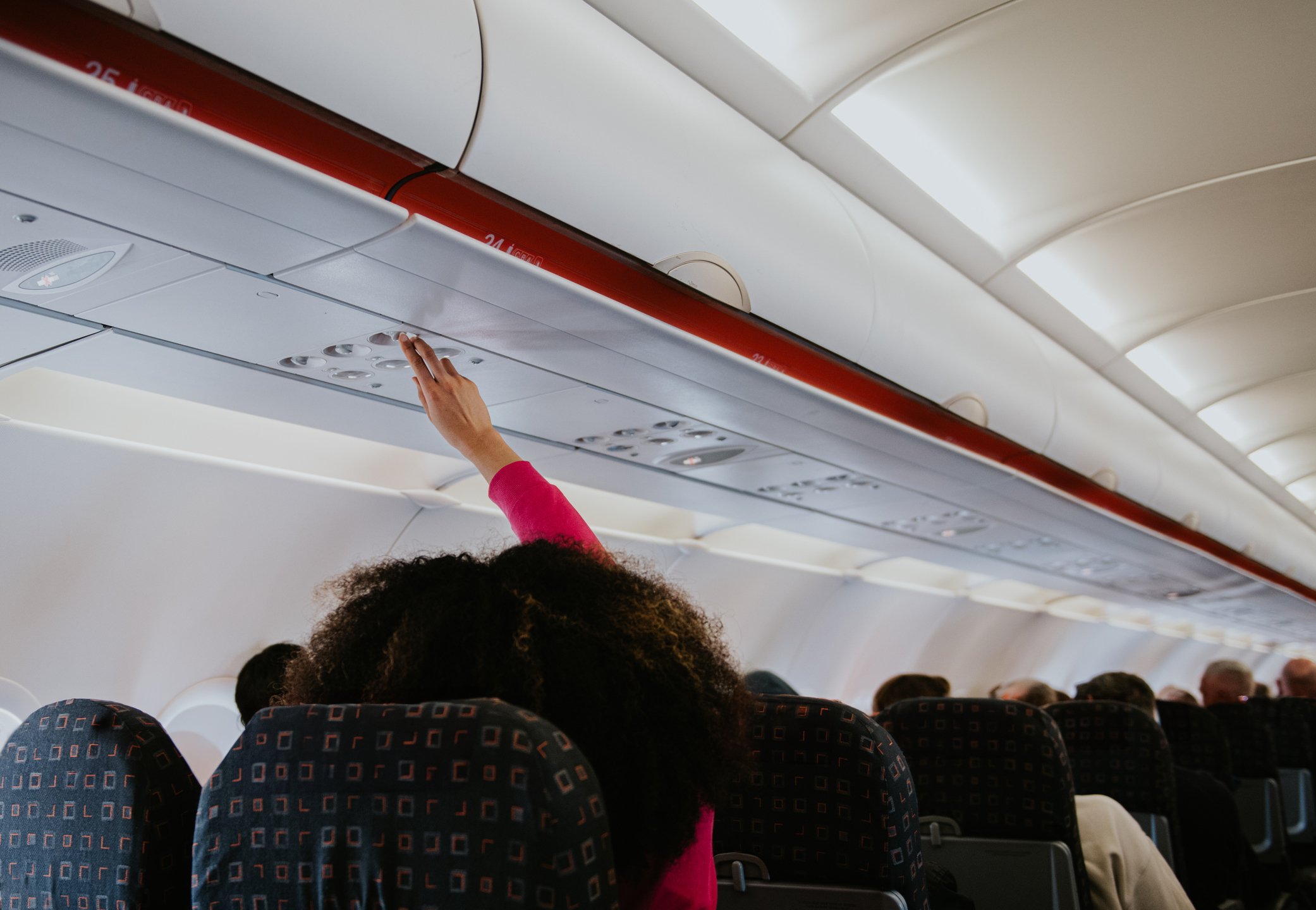 Passenger in airplane cabin reaching for overhead bin