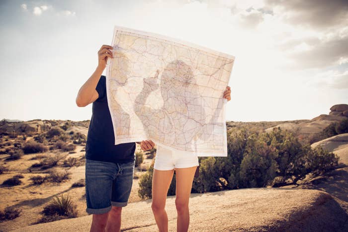 Two people standing outdoors holding a large map, face obscured by the map, in a desert-like setting