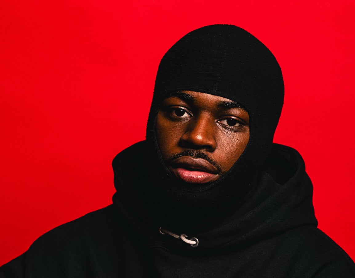 Person in black hoodie and beanie against red background