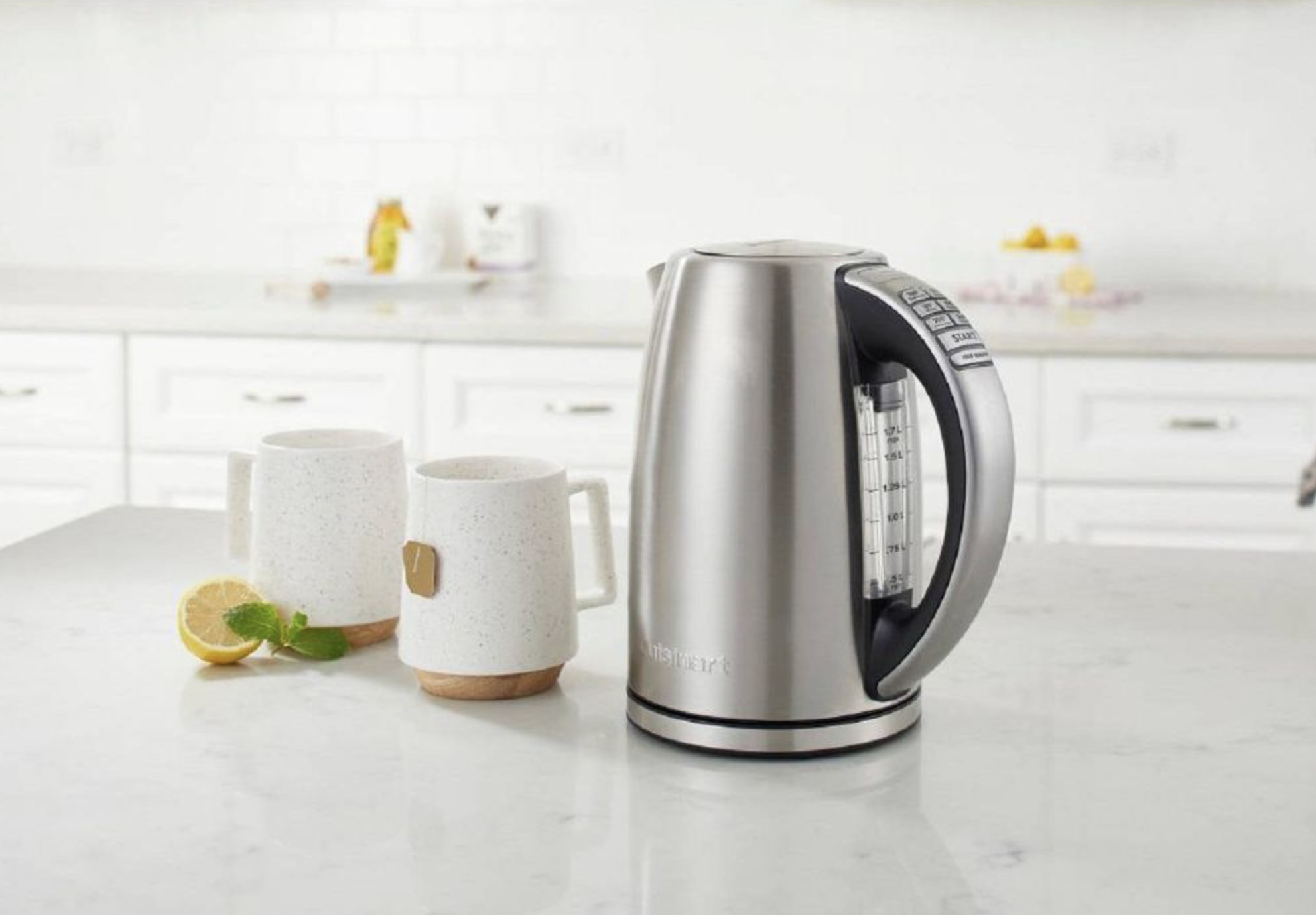 Stainless steel electric kettle on kitchen counter beside two mugs and a sliced lemon