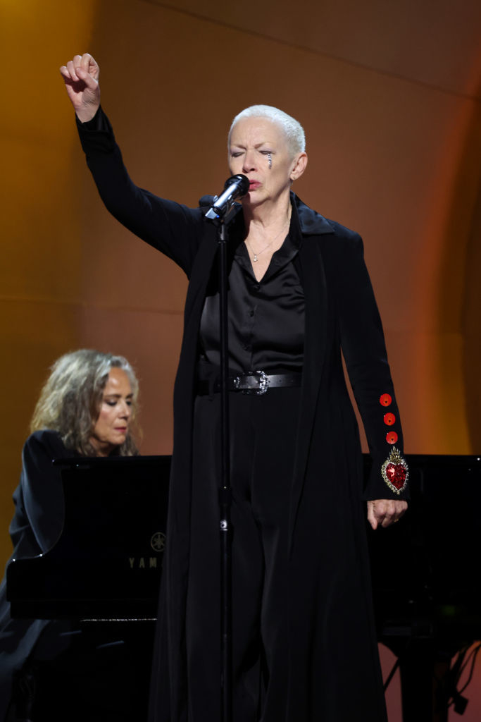 Annie singing on stage, arm raised with a pianist in background