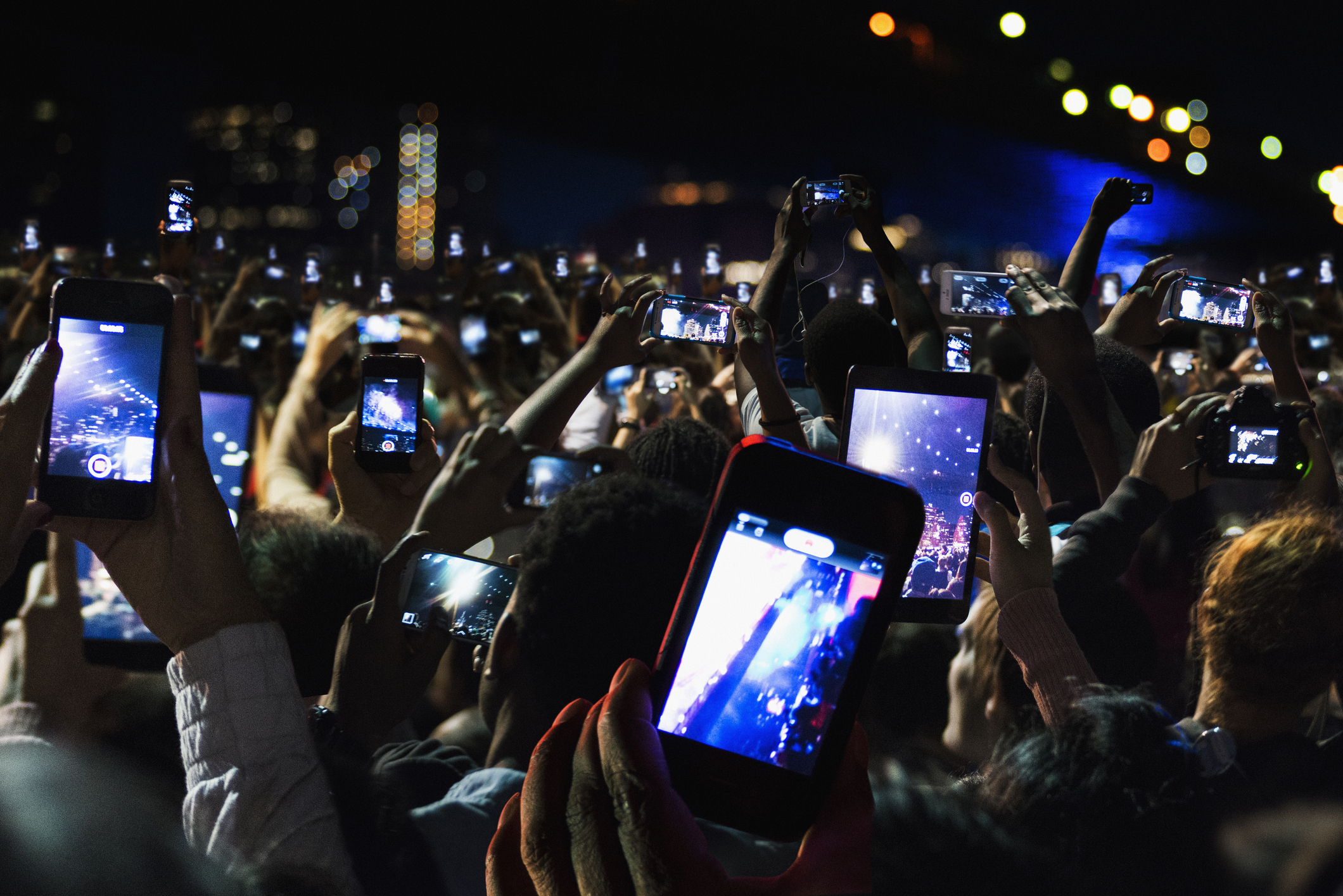 Crowd holding up phones to capture a concert stage at night