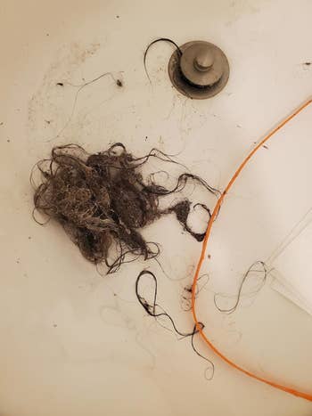 Hair clogged in a shower drain next to an orange drain snake