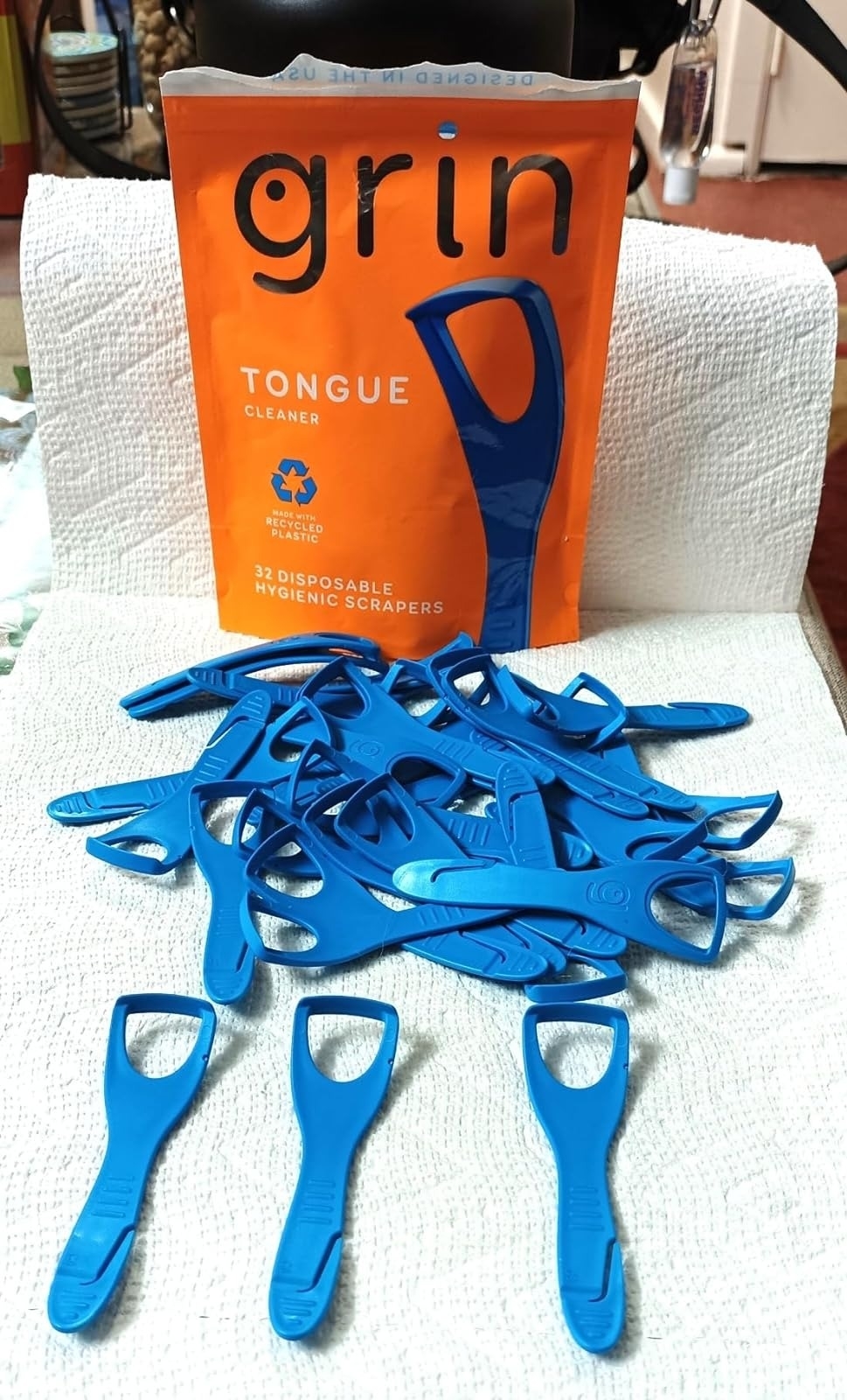 A pack of Grin tongue cleaners and several individual blue scrapers displayed on a surface